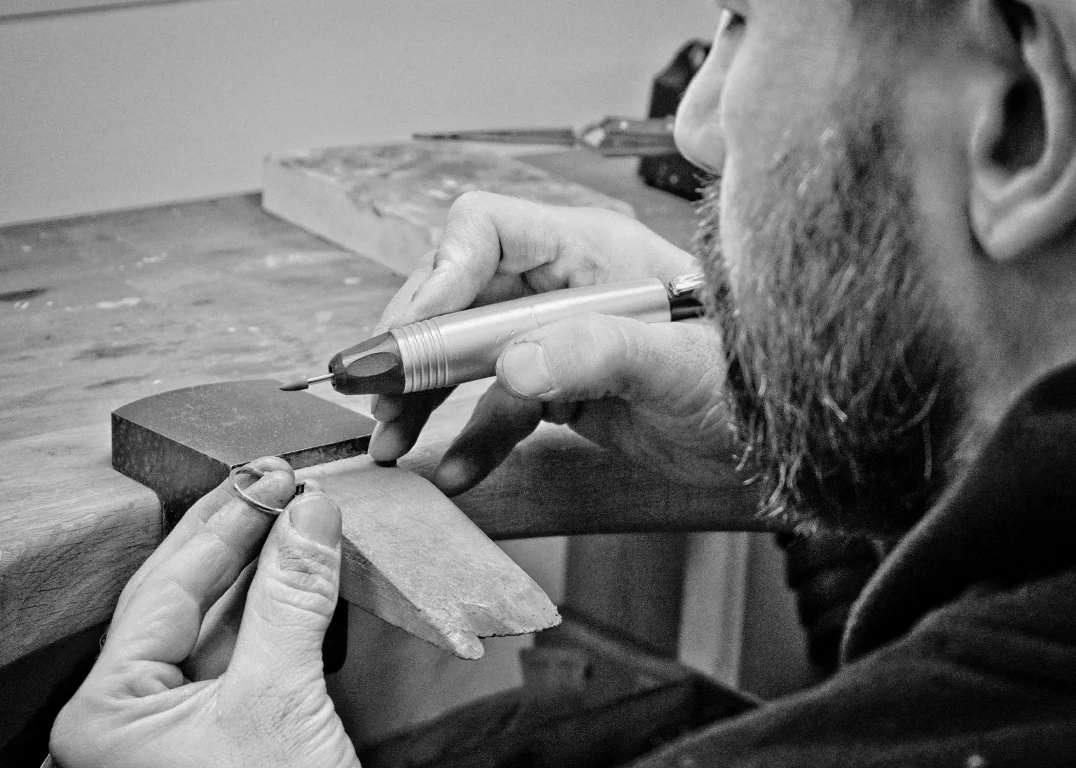 A jeweller at the bench working on a ring held against a bench peg with a handpiece.